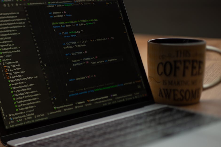 A close-up view of a laptop displaying lines of programming code, placed on a wooden desk illuminated by soft indoor lighting. Next to the laptop, there is a ceramic coffee mug with a beige background